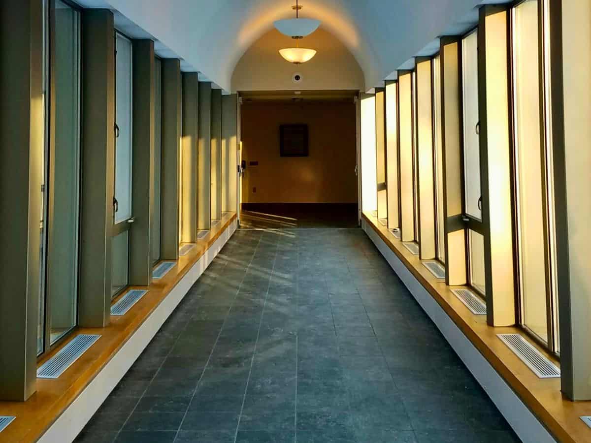 A quiet university hallway with soft window light and pendant lamps, symbolizing structure and protected time for faculty sabbatical leave.